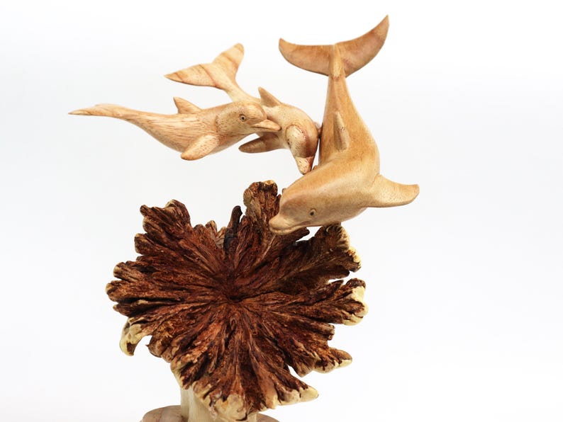 May include: A wooden sculpture of three dolphins leaping out of the water, with a brown wooden base that resembles coral.