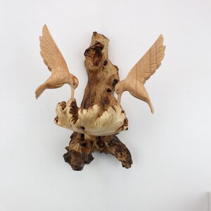 May include: A wooden sculpture of two birds perched on a branch. The birds are carved in a realistic style and have detailed feathers. The branch is also carved in a realistic style and has a rough, textured surface.
