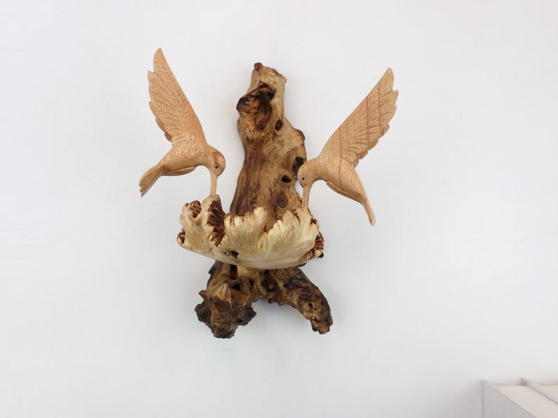 May include: A wooden sculpture of two birds perched on a branch. The birds are carved in a realistic style and have detailed feathers. The branch is also carved in a realistic style and has a rough, textured surface.
