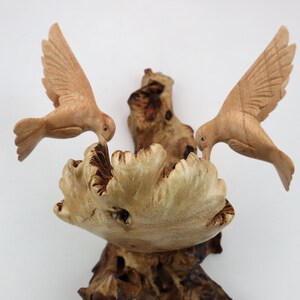 May include: A wooden sculpture of two birds perched on a branch. The birds are carved in a realistic style and have detailed feathers. The branch is also carved in a realistic style and has a rough texture.