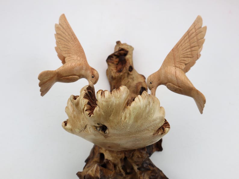 May include: A wooden sculpture of two birds perched on a branch. The birds are carved in a realistic style and have detailed feathers. The branch is also carved in a realistic style and has a rough texture.