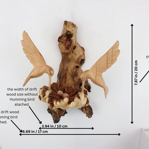 May include: A wooden sculpture of two hummingbirds perched on a driftwood branch with a nest. The sculpture is 7.87 inches tall and 6.69 inches wide.