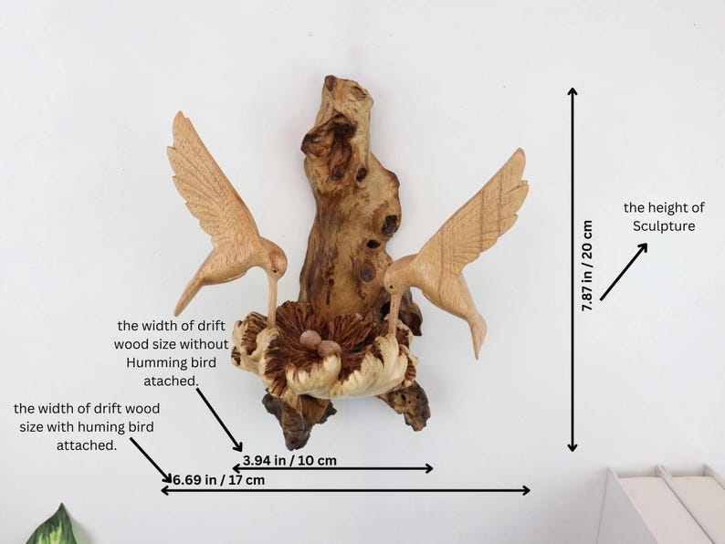 May include: A wooden sculpture of two hummingbirds perched on a driftwood branch with a nest. The sculpture is 7.87 inches tall and 6.69 inches wide.