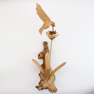 May include: A wooden sculpture of a hummingbird perched on a flower. The sculpture is made of natural wood and has a rustic, hand-crafted look.