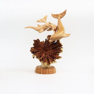 May include: A wooden sculpture of three dolphins leaping out of the water, with a brown wooden base that resembles coral.