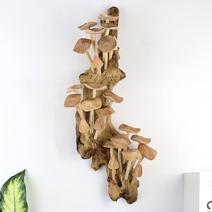 Könnte beinhalten: Eine Holzskulptur von Pilzen, die auf einem Stück Treibholz wachsen. Die Pilze haben hellbraune Kappen und Stiele, und das Treibholz ist dunkelbraun. Die Skulptur ist an einer weißen Wand befestigt.