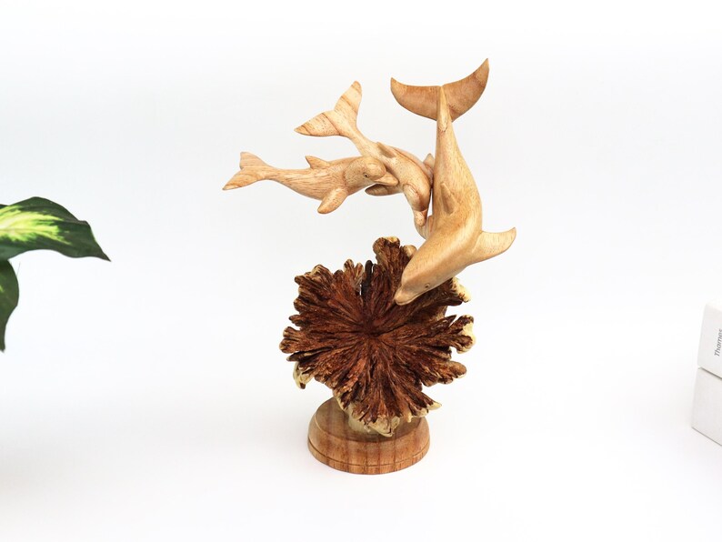 May include: A wooden sculpture of three dolphins leaping out of a coral reef. The dolphins are carved in a realistic style and are painted in shades of brown. The coral reef is carved in a more abstract style and is painted in shades of brown and red.