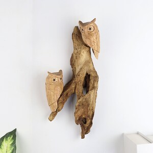 May include: Two wooden owls perched on a piece of driftwood. The owls are carved with detailed features and have a natural wood finish.