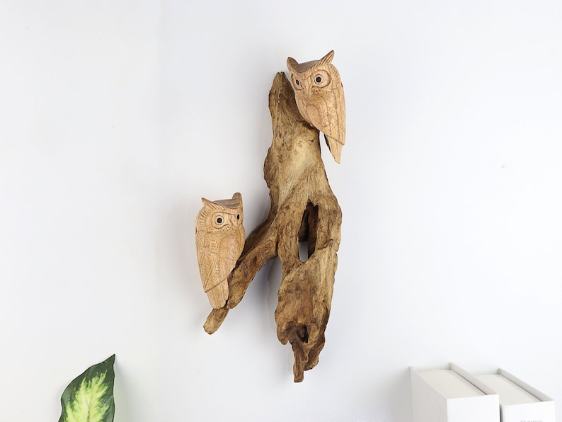 May include: Two wooden owls perched on a piece of driftwood. The owls are carved with detailed features and have a natural wood finish.