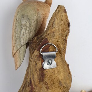 May include: A wooden bird sculpture with a metal hanging hook on the back. The bird is carved in a natural wood colour and has a weathered look.