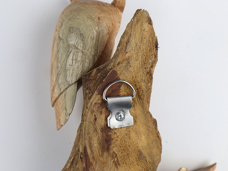 May include: A wooden bird sculpture with a metal hanging hook on the back. The bird is carved in a natural wood colour and has a weathered look.