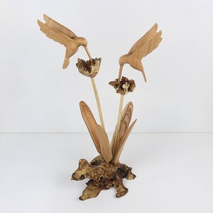 May include: A wooden sculpture of two hummingbirds perched on a branch with flowers. The sculpture is made of natural wood and has a rustic finish.