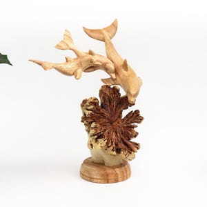 May include: A wooden sculpture of three dolphins leaping over a coral reef. The dolphins are carved in a realistic style and the coral reef is detailed with intricate carvings.