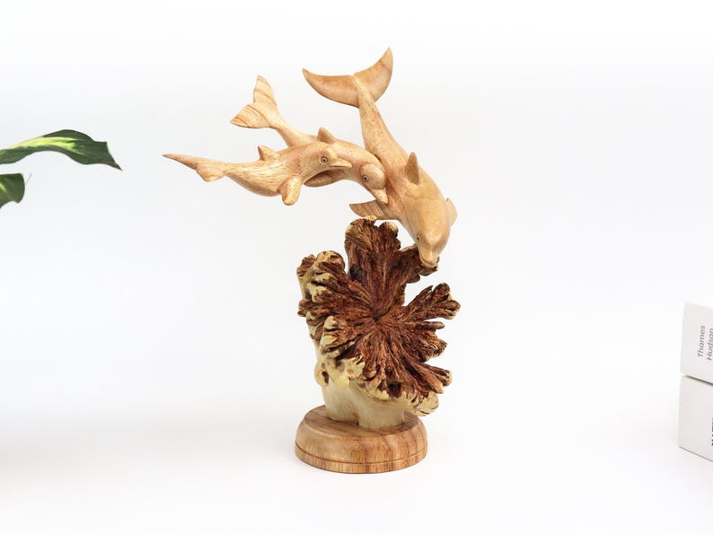 May include: A wooden sculpture of three dolphins leaping over a coral reef. The dolphins are carved in a realistic style and the coral reef is detailed with intricate carvings.