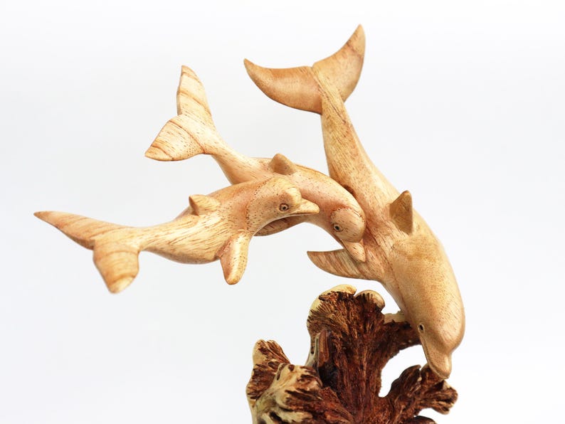 May include: A wooden sculpture of three dolphins leaping out of the water. The dolphins are carved in a realistic style and are painted in shades of brown. The sculpture is mounted on a wooden base that resembles a coral reef.