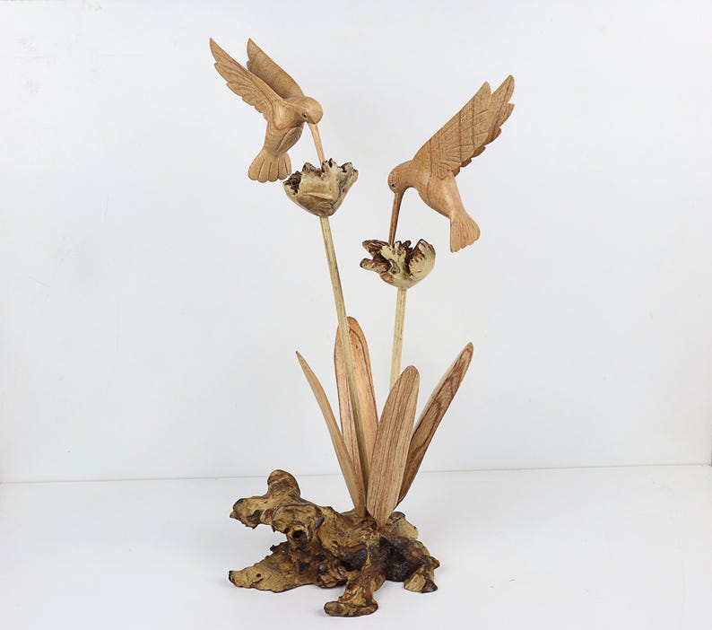 May include: Hand-carved wooden sculpture of two hummingbirds perched on a flower with leaves and a wooden base.