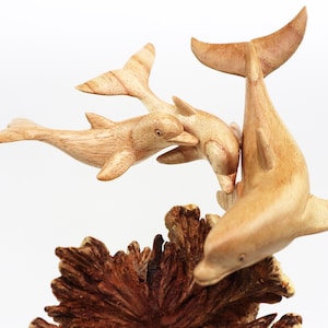 May include: A wooden sculpture of three dolphins leaping out of the water. The dolphins are carved in a realistic style and are painted in shades of brown. The sculpture is set on a base of carved wood that resembles coral.