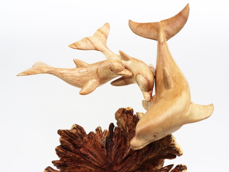 May include: A wooden sculpture of three dolphins leaping out of the water. The dolphins are carved in a realistic style and are painted in shades of brown. The sculpture is set on a base of carved wood that resembles coral.