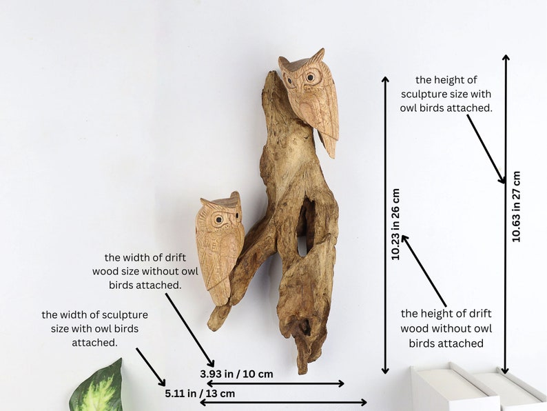 May include: A wooden sculpture of two owls perched on a driftwood branch. The sculpture measures 27 cm tall and 26 cm wide. The owls are carved in detail and have a natural wood finish.