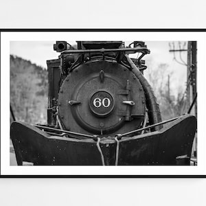 May include: Black and white photograph of a vintage steam locomotive. The front of the train is centered, showcasing the large circular boiler with the number "60" in the center. The image is framed in a black border.