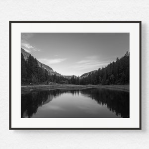 May include: A black and white photograph of a lake reflecting the surrounding trees and mountains.
