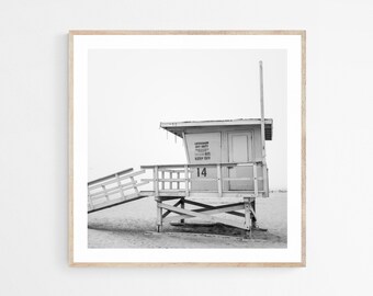 May include: Black and white photograph of a lifeguard station on a beach. The station is a light color with the number 14 visible. The text "LIFEGUARD ON DUTY" and "KEEP OFF" are also visible. The image is framed in a light wood frame.