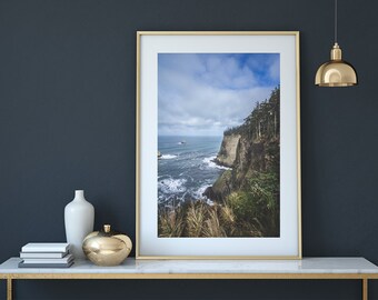 May include: A framed photograph of a rocky coastline with a blue sky and ocean. The photo is hanging on a dark blue wall above a white marble table with gold accents.
