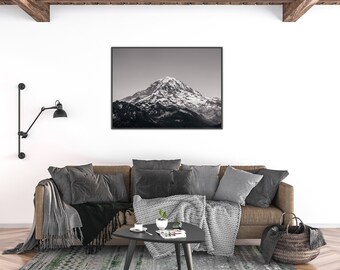 May include: A black and white framed print of a snow-capped mountain hangs above a brown sofa with gray pillows and blankets. A black side table holds a plant and coffee cup. A black lamp is mounted on the wall.