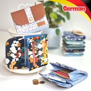 May include: A collection of fabric wallets featuring various patterns including a brown and grey chevron design with a 'NICE!' label, a dark blue floral print with rabbits, and a blue polka dot interior. Several wallets are stacked in the background.