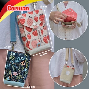 Könnte beinhalten: Zwei Umhängetaschen mit verstellbaren Riemen. Eine Tasche zeigt ein rotes Erdbeermuster auf cremefarbenem Grund mit dem Text QUEEN OF BERRIES und misst 19 cm mal 13 cm. Die andere Tasche hat ein dunkelblaues Blumenmuster und ist 11,5 cm breit.