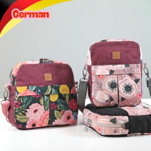 May include: Three bags with a floral pattern featuring pink, red, yellow, and green flowers on dark backgrounds. The bags have maroon panels, silver zippers, and grey straps. Each bag features a small square brown label on the front panel.