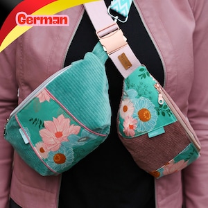 Pode incluir: Uma bolsa transversal de dois compartimentos em veludo cotelê azul-petróleo com estampa floral em rosa, branco e azul. A bolsa possui uma alça ajustável rosa claro com fivela de plástico, uma pequena etiqueta de couro marrom e uma etiqueta azul PERFECT.
