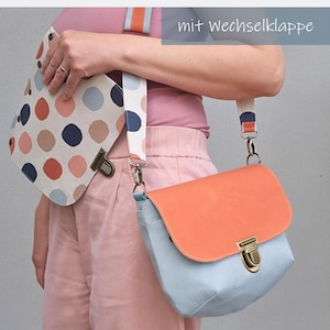 May include: A light blue crossbody bag with an orange flap and a brass-toned metal clasp. The bag features a detachable strap with a blue, orange, and white polka dot pattern. An additional interchangeable flap with a polka dot print is included.