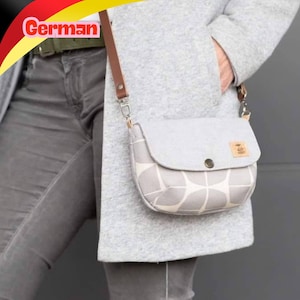 Könnte beinhalten: Eine kleine Umhängetasche mit einem hellgrau-weißen geometrischen Muster im unteren Bereich und einer einfarbig hellgrauen Klappe. Die Tasche hat einen braunen Lederriemen mit silberfarbenen Metallbeschlägen und ein kleines rechteckiges Logo.