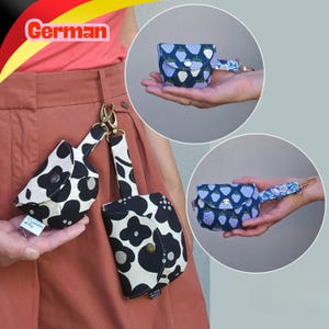 Könnte beinhalten: Zwei kleine Stoffbeutel mit Druckknöpfen und Metallclips. Ein Beutel hat ein schwarz-weißes Blumenmuster, der andere einen blau-weißen Erdbeerdruck. Beide Artikel verfügen über ein kurzes Band und ein kleines weißes Etikett mit Markenaufschrift.