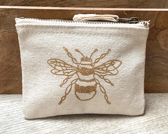 May include: A small, off-white canvas pouch with a zipper closure. The pouch features a gold-colored bee design.