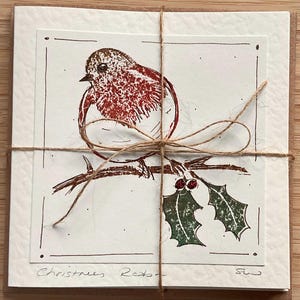 May include: A set of Christmas cards tied with twine. Each card features a red robin illustration perched on a branch with holly. The words "Christmas Robin" are handwritten at the bottom of the card.