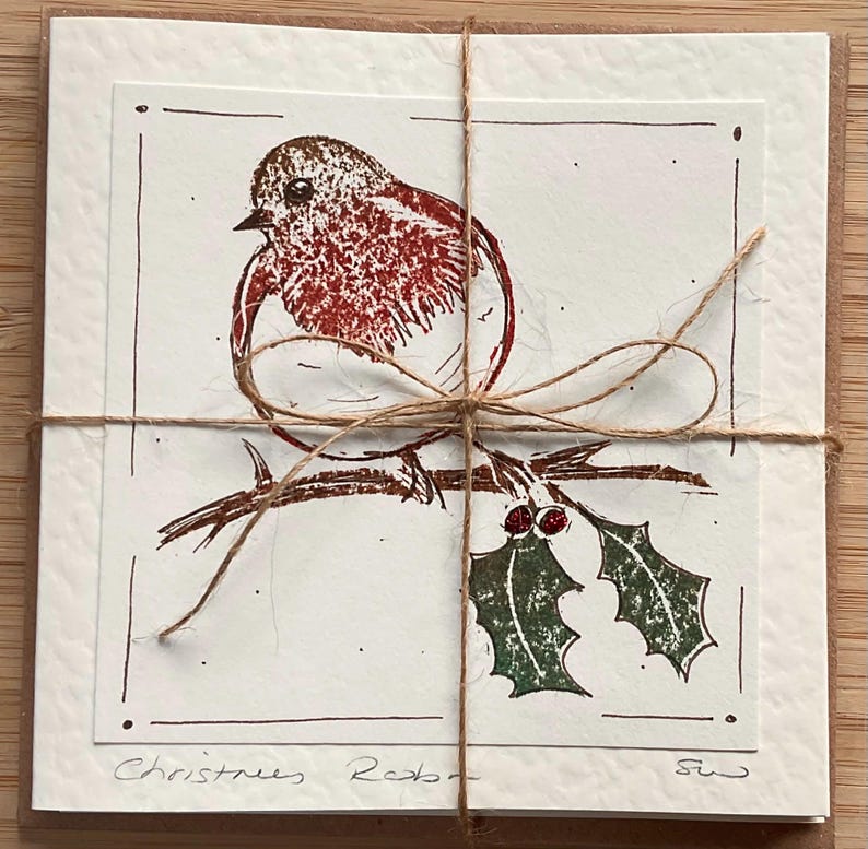 May include: A set of Christmas cards tied with twine. Each card features a red robin illustration perched on a branch with holly. The words "Christmas Robin" are handwritten at the bottom of the card.