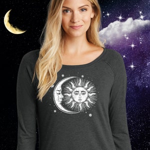 May include: A dark gray long-sleeved shirt with a white graphic of a crescent moon and sun with a face. The graphic is surrounded by small white stars.