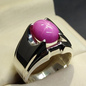 May include: A silver ring featuring a pink star sapphire gemstone. The ring has a distinctive design with a pointed setting.