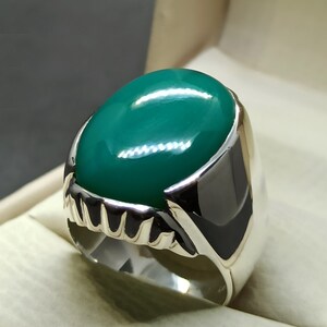 May include: A silver ring featuring a large, oval-shaped green gemstone. The ring has a detailed, textured band.