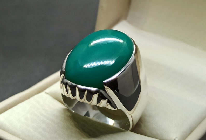May include: A silver ring featuring a large, oval-shaped green gemstone. The ring has a detailed, textured band.