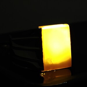 May include: A gold ring with a large, square, yellow gemstone. The gemstone is illuminated from within, creating a warm glow.