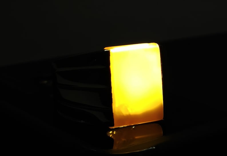 May include: A gold ring with a large, square, yellow gemstone. The gemstone is illuminated from within, creating a warm glow.