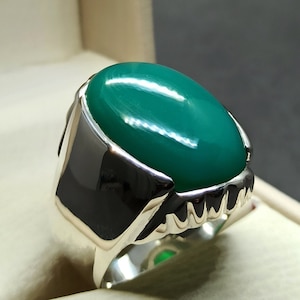 May include: A silver ring featuring a large, oval-shaped green gemstone. The ring has a detailed, textured band.