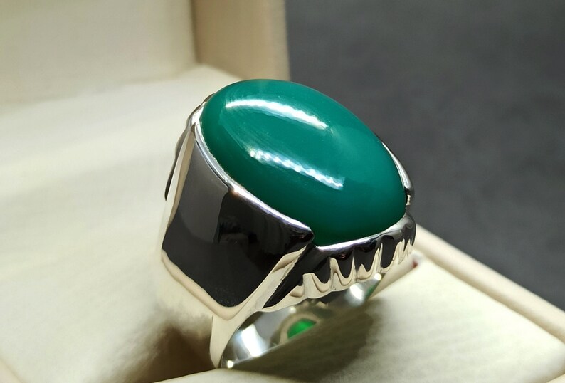May include: A silver ring featuring a large, oval-shaped green gemstone. The ring has a detailed, textured band.