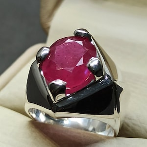 May include: A silver ring with a large, faceted, red ruby gemstone set in a black metal bezel.