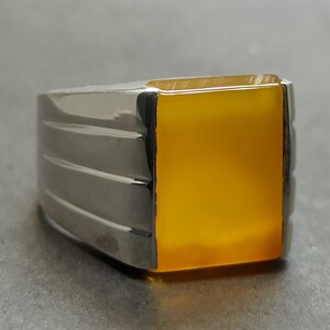 May include: A silver ring with a square, yellow gemstone.