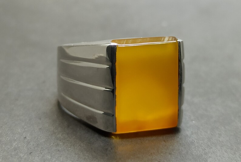 May include: A silver ring with a square, yellow gemstone.