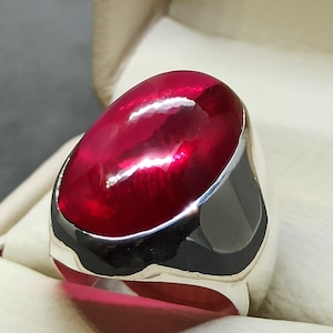 May include: A silver ring with a large, oval-shaped, deep red gemstone.